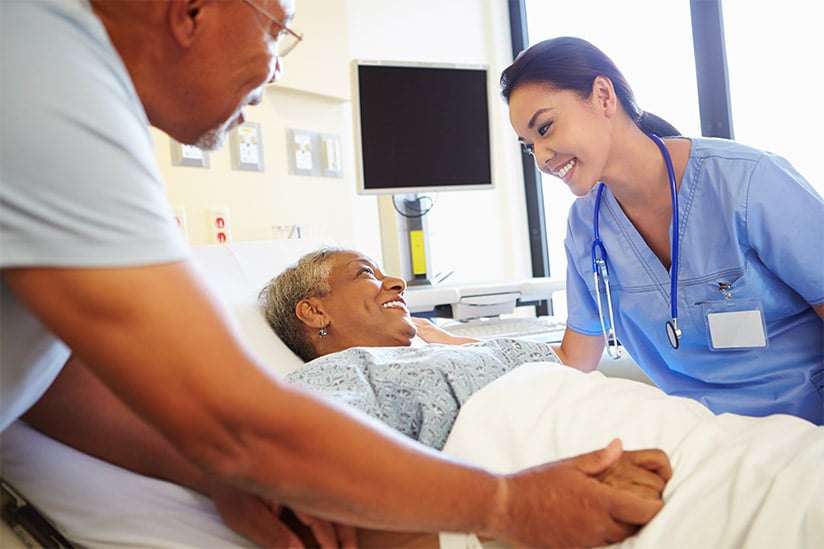 Smiling female medical practitioner attends to smiling patient in hospital bed