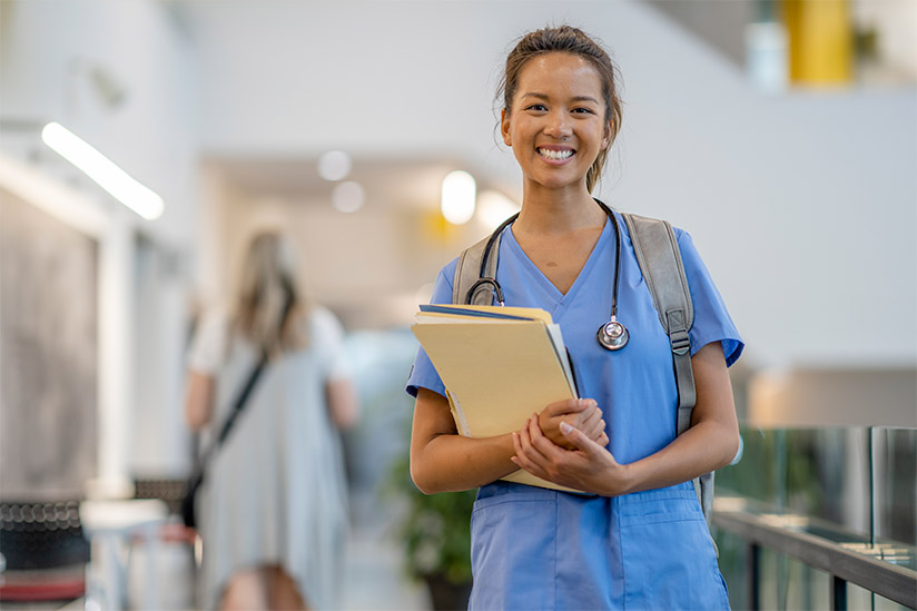 A woman in med school poses for a portrait while walking through the halls with her study materials.